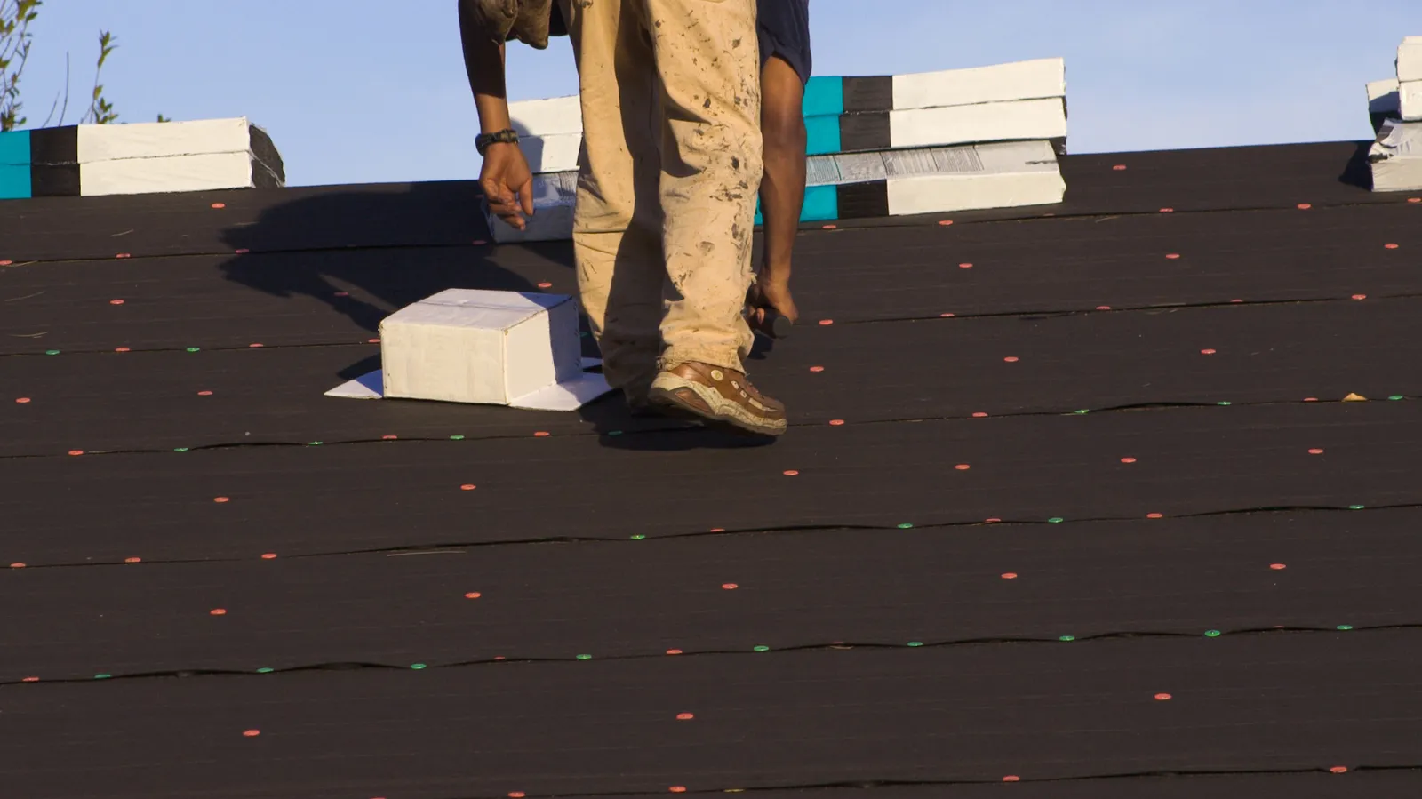 A roofer walking across underlayment near stacked shingle bundles